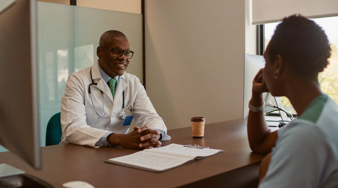 A doctor talking with a patient across a consulting-room desk